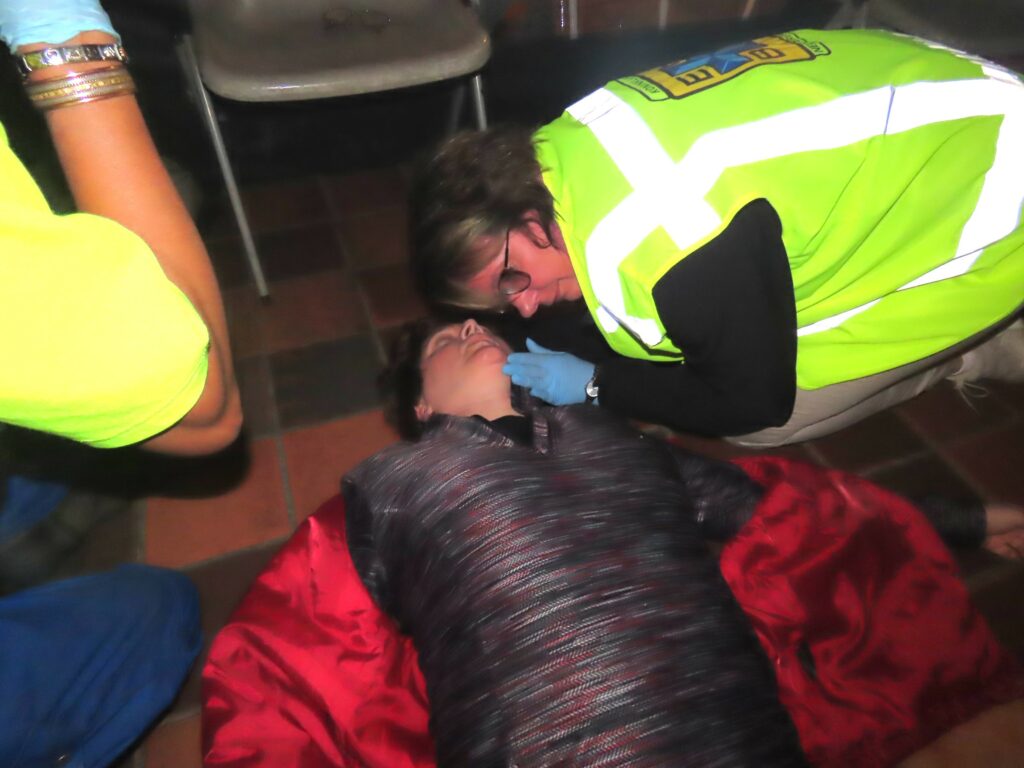 SO7 EHBO hulpverlener controleert ademhaling bij feestganger met na epilepsie aanval.